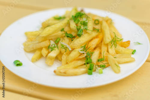 French fries on a plate on a yellow wooden background.