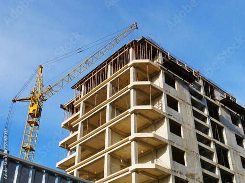 Construction crane near building. Concrete building under construction against blue sky. Construction site.