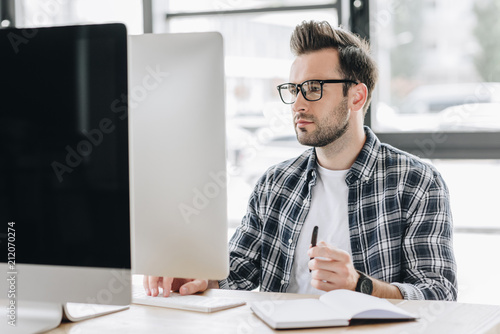 focused young man in eyeglasses working with desktop computer photo