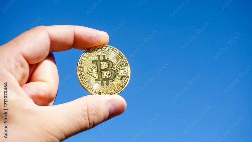 Hand mit Bitcoin Münze vor blauem Himmel Hand mit Bitcoin Münze vor blauem Himmel