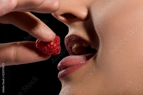 girl mouth eating raspberry on black background