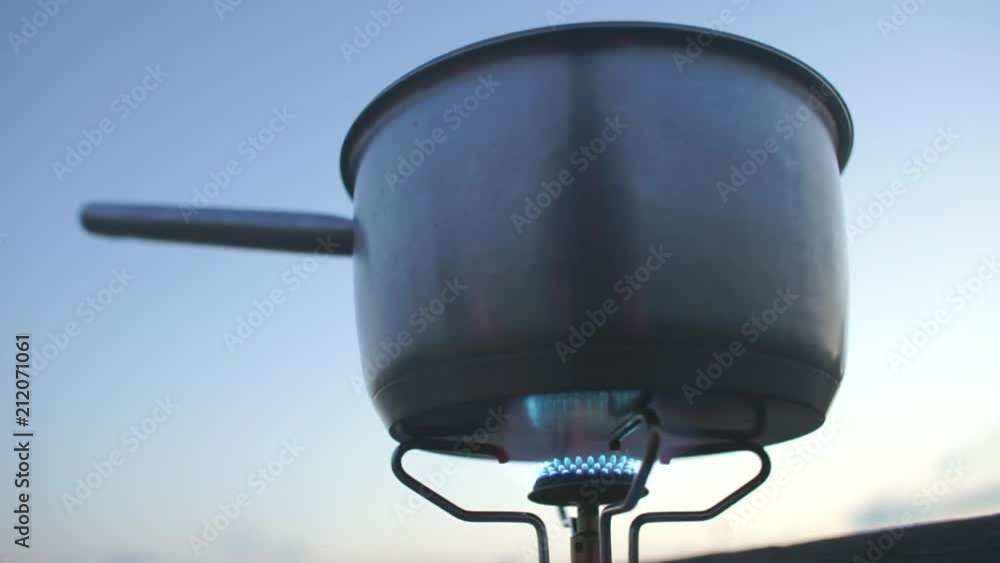 A metal pot with a handle stands and is heated on a gas burner against the sky in the mountains. Self-isolation, quarantine of viral infection COVID 19. Healthy lifestyle. A metal pot with a handle stands and is heated on a gas burner against the sky in the mountains. Self-isolation, quarantine of viral infection COVID 19. Healthy lifestyle.