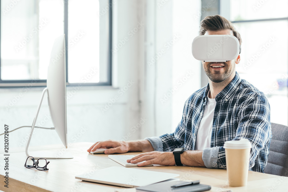 smiling young man in virtual reality headset using desktop computer at workplace smiling young man in virtual reality headset using desktop computer at workplace