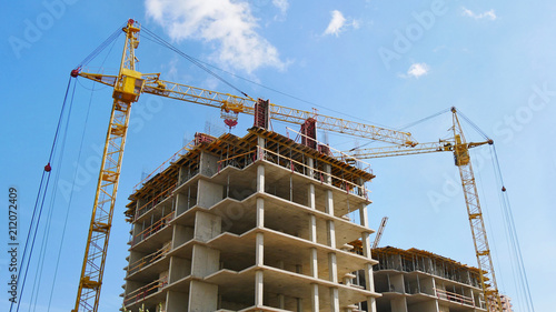 Construction site background. Two tower cranes near building. Building cranes and buildings under construction against blue sky