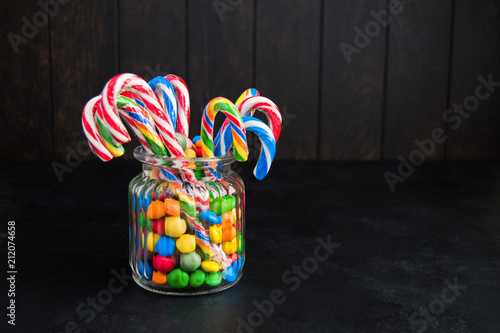 Candy canes with colorful sweets in jar with copy space