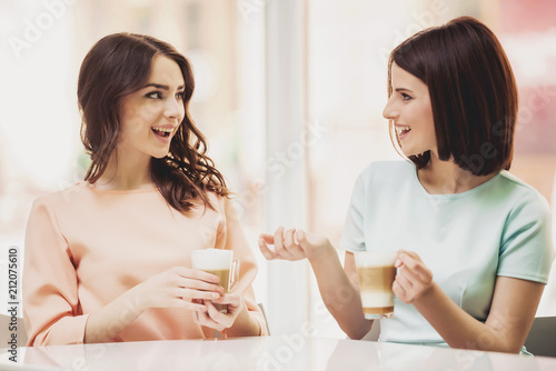 Two Girls Chatting in Cafeteria with Cups of Coffee.