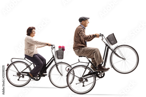 Elderly woman and an elderly man riding bicycles with the elderly man doing a wheelie