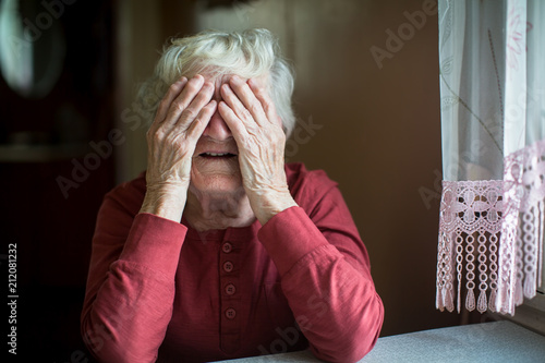 Elderly woman covers face with wrinkled hands.