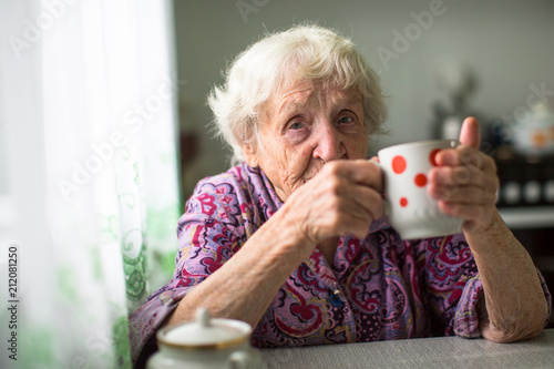 An elderly woman drinks tea sitting in the kitchen. photo