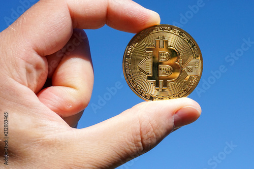 Hand mit goldener Bitcoin Münze zwischen den Fingern