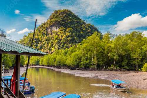 A wooden boat dock and moored motorboats in front of a beautiful limestone hill at the Kilim Jetty, located at the north eastern edge of Langkawi on Kilim river, Malaysia. One motorboat is returning.