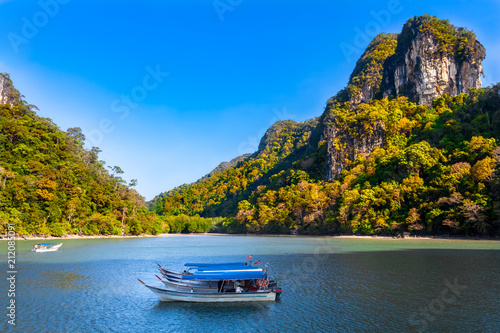 Magnificent scenery of the Kilim Geoforest Park in Langkawi, Malaysia. A few motorboats are moored in the shaded area of the river and in the background are mangrove trees and limestone hills. photo