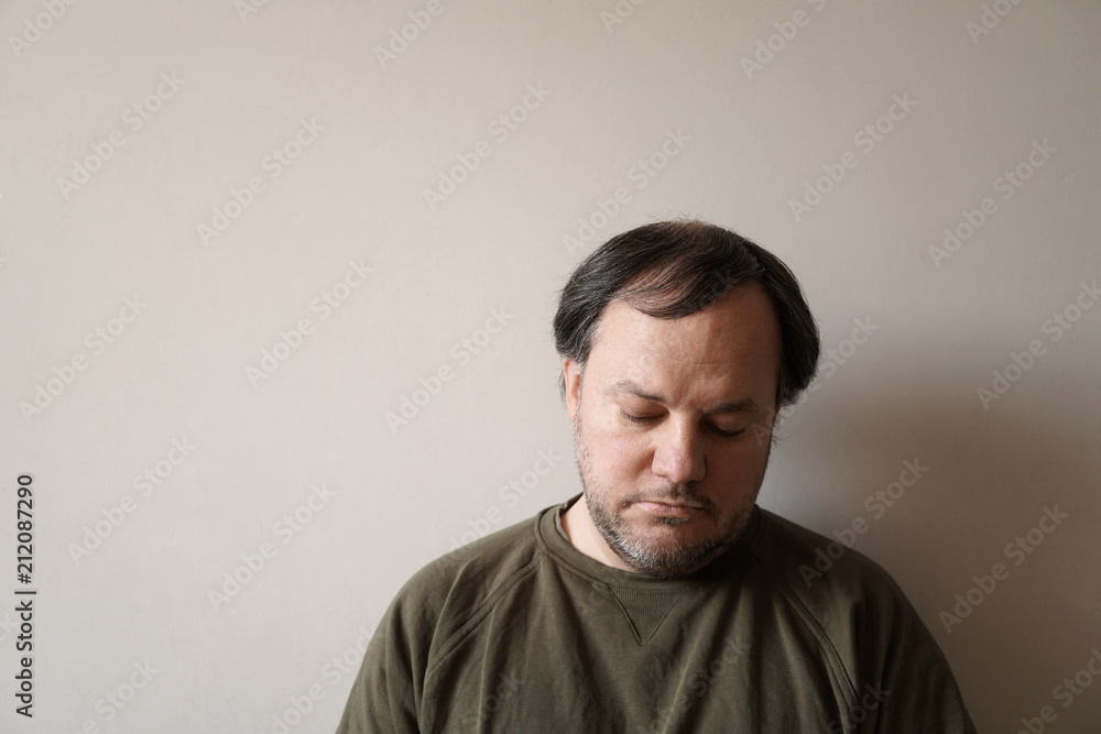 depressed man in his forties leaning against wall with copy space. depression or midlife crisis concept.