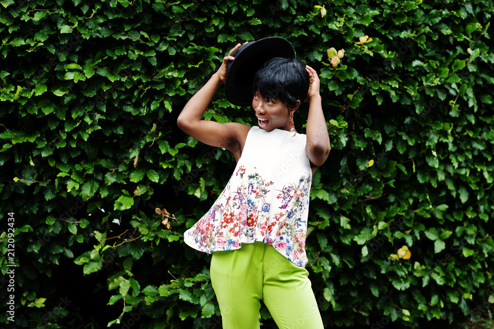 Amazing african american model woman in green pants and black hat posed with different emotions at park. Amazing african american model woman in green pants and black hat posed with different emotions at park.