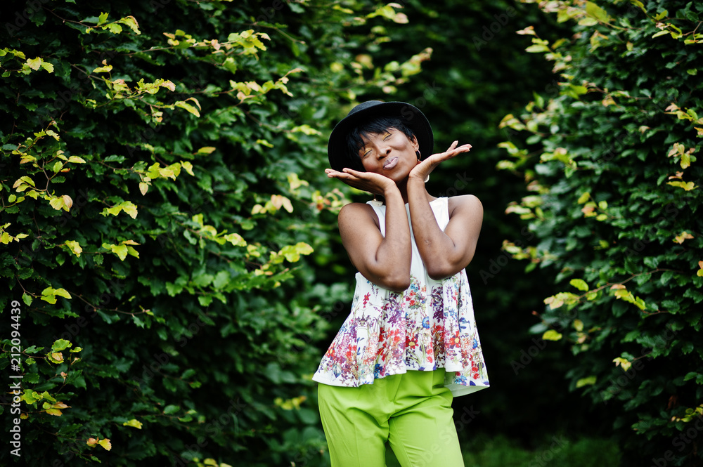 Amazing african american model woman in green pants and black hat posed at park. Amazing african american model woman in green pants and black hat posed at park.