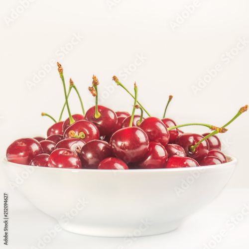 Ripe cherry lies in a white bowl on a white background