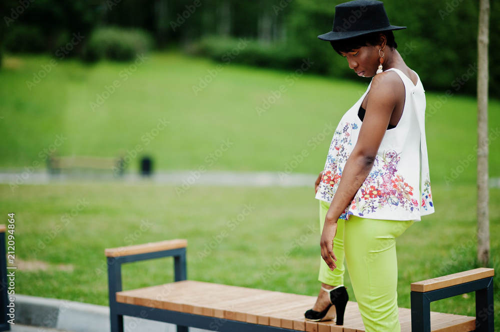 Obraz premium Amazing african american model woman in green pants and black hat posed at park.