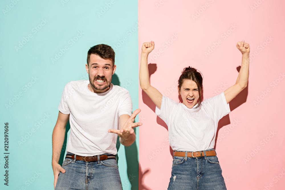 Closeup portrait of young couple, man, woman. One being excited happy smiling, other serious, concerned, unhappy on pink and blue background. Emotion contrasts Closeup portrait of young couple, man, woman. One being excited happy smiling, other serious, concerned, unhappy on pink and blue background. Emotion contrasts
