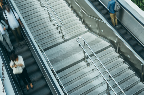 People on stairs and moving escalator at the interchange station near business and commercial center in Paris. Urban scene, city life, public transport hub and traffic concept. Blurred background