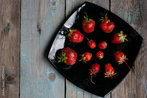 top view Red ripe strawberries on a black plate on a wooden table top view