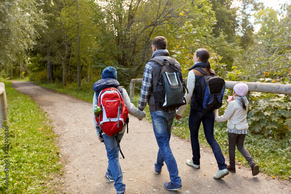 family, tourism and hiking concept - happy mother, father, son and daughter with backpacks walking in woods family, tourism and hiking concept - happy mother, father, son and daughter with backpacks walking in woods