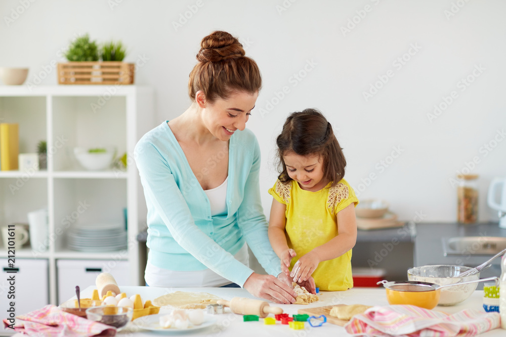 Fototapeta premium family, cooking and people concept - happy mother and little daughter with molds making cookies from dough at home kitchen