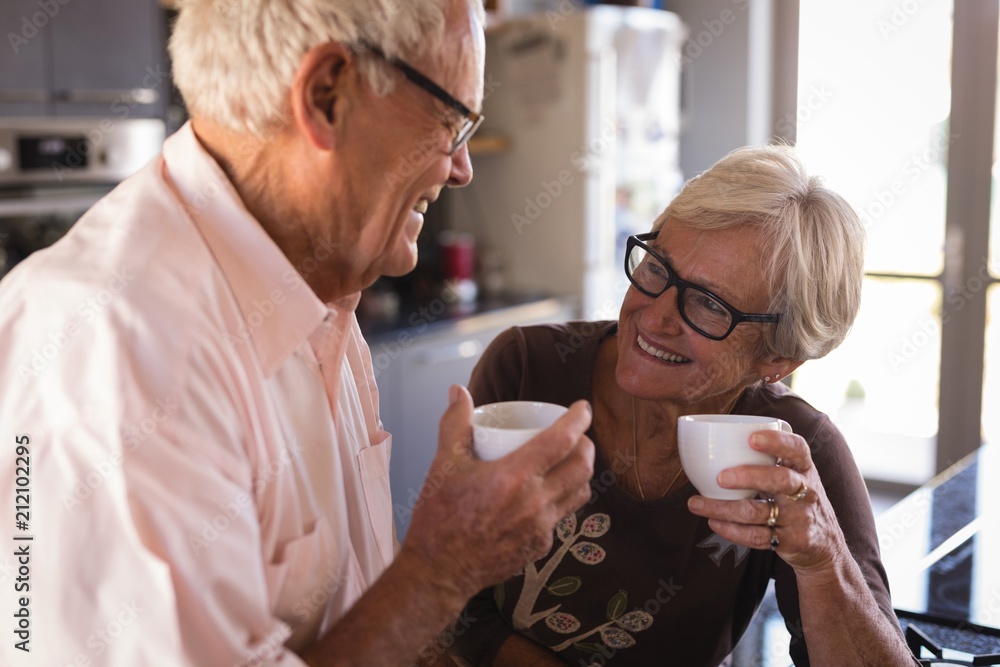 Senior couple smiling while having coffee in kitchen Senior couple smiling while having coffee in kitchen