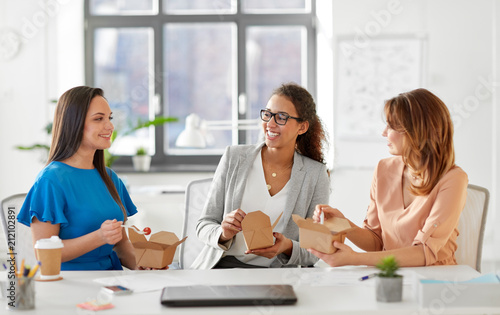 business lunch and people concept - happy businesswomen eating take out food at office