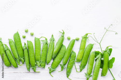 Pods of green peas on a white wooden surface close up, top view, copy space