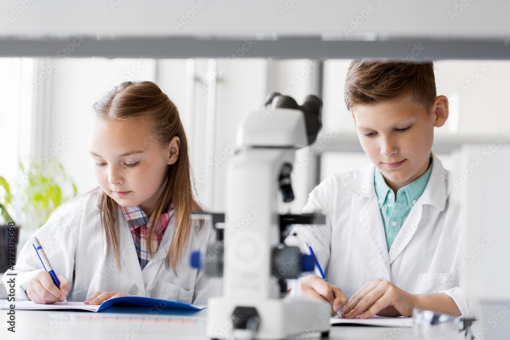 education, science and children concept - kids studying chemistry at school laboratory and writing to workbooks education, science and children concept - kids studying chemistry at school laboratory and writing to workbooks