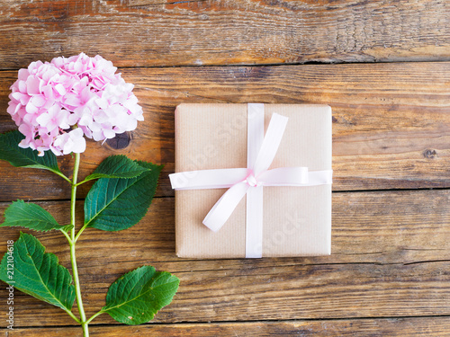 Geschenkspaket mit rosa Schleife und einer Blume auf einem Holztisch