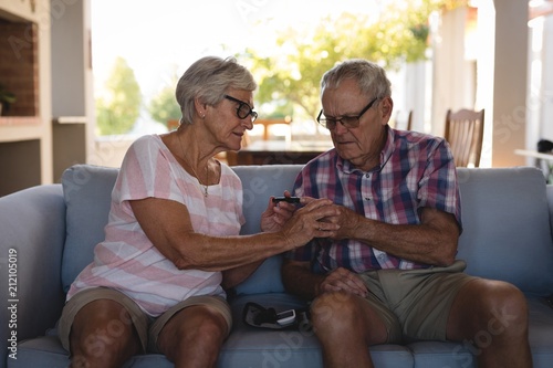 Senior couple checking blood sugar with glucometer in living photo