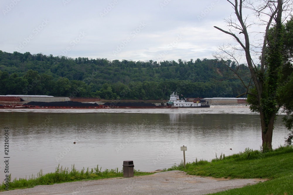 The large barge going up the flowing river on a cloudy day.