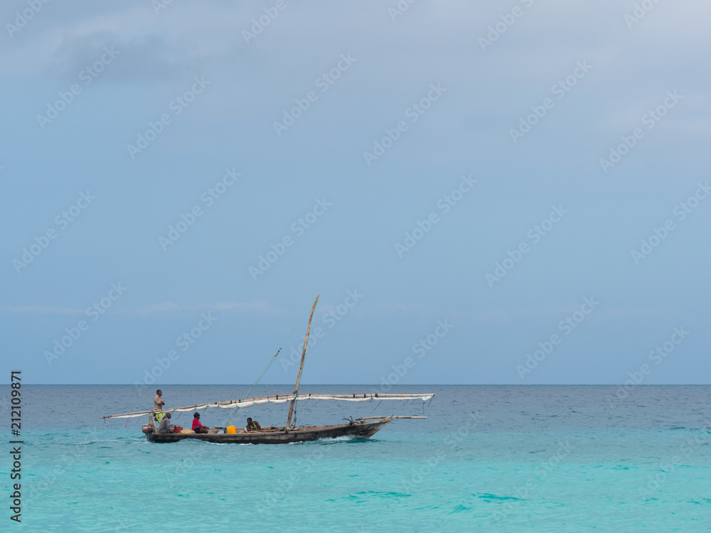 Fototapeta premium Fisherman fishing and sails on a wooden boat on clear blue water along a tropical exotic beach in Africa. Indian Ocean, Zanzibar