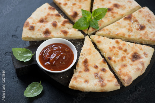 Black wooden serving board with sliced ossetian pie, dipping sauce and fresh green basil, studio shot on a black stone surface photo