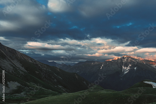 mountain peak sunset landscape with gloomy dramatic mainly cloudy sky and orange and red sun beams © kravtzov