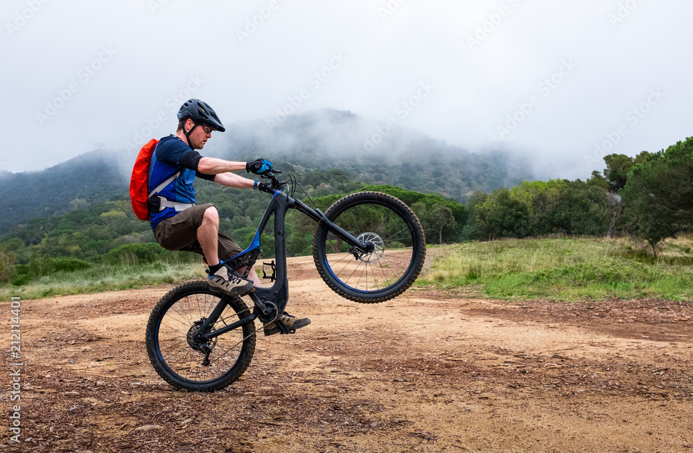 Young man doing a wheelie on a black and blue electric mountain bike