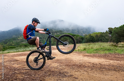 Fotografie Young man doing a wheelie on a black and blue electric mountain bike