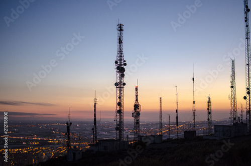communication tower. cell, radio and television antennas on top of a mountain and below a lit coastal village photo