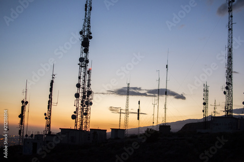 communication tower. cell, radio and television antennas on top of a mountain and below a lit coastal village photo