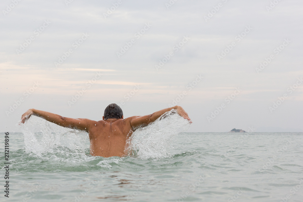 Young man determined to reach a small island on the background by swimming the butterfly stroke technique in Koh Pha Ngan, Thailand. Summer vacation, water sport concept