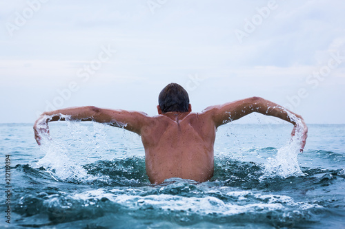 Fotografija Back of young man with arms open training on the open sea practicing the butterfly swimming technique in the island of Koh Pha Ngan, Thailand