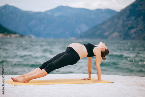 Pregnant woman doing yoga. Relaxation in the nature near the water