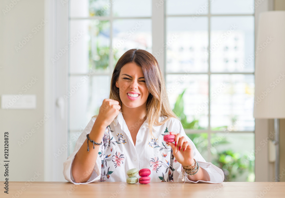 Young woman at home eating macarons annoyed and frustrated shouting with anger, crazy and yelling with raised hand, anger concept Young woman at home eating macarons annoyed and frustrated shouting with anger, crazy and yelling with raised hand, anger concept