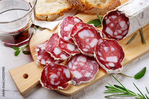 Quadro su tela Salami, bread and red wine with cutting board on white plaster background