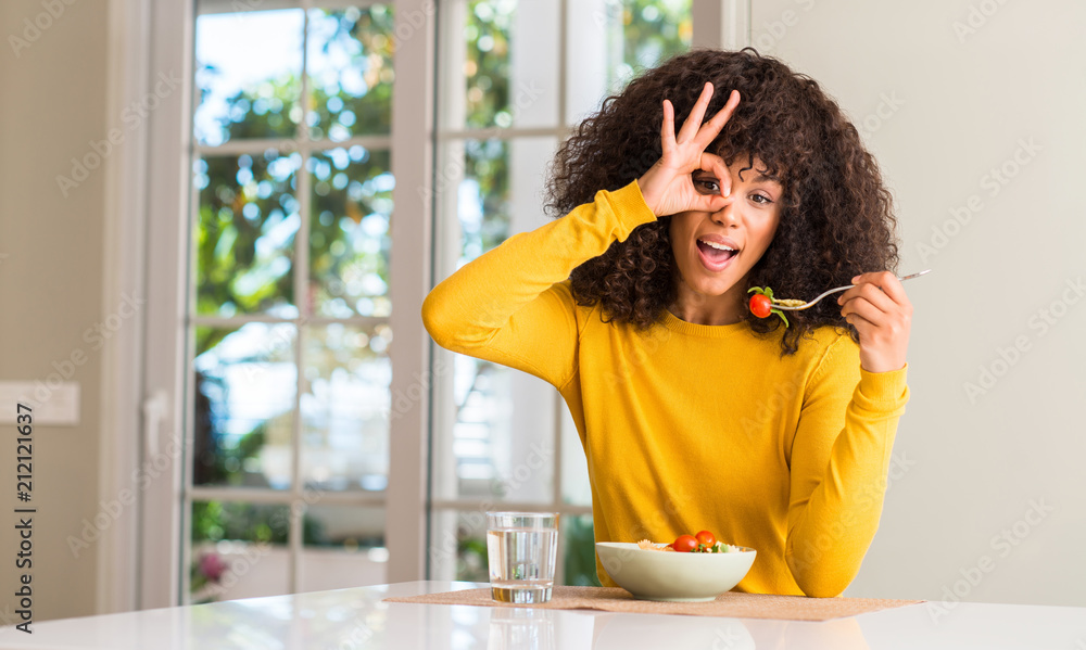 African american woman eating pasta salad with happy face smiling doing ok sign with hand on eye looking through fingers African american woman eating pasta salad with happy face smiling doing ok sign with hand on eye looking through fingers