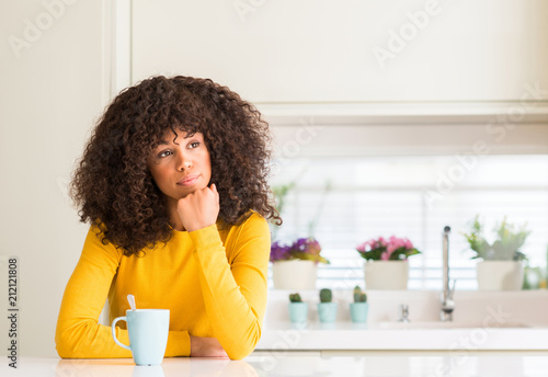 Beautiful african american woman holding a cup of coffee at home serious face thinking about question, very confused idea