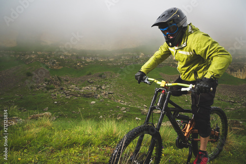 A man in a mountain helmet riding a mountain bike rides around the beautiful nature in cloudy weather. downhill