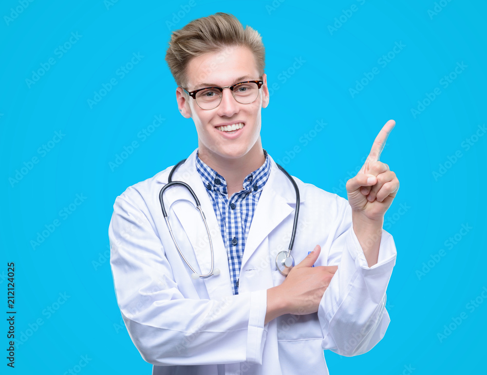 Young handsome blond doctor very happy pointing with hand and finger to the side Young handsome blond doctor very happy pointing with hand and finger to the side