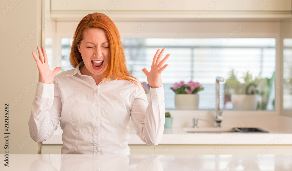Redhead woman at kitchen celebrating mad and crazy for success with arms raised and closed eyes screaming excited. Winner concept Redhead woman at kitchen celebrating mad and crazy for success with arms raised and closed eyes screaming excited. Winner concept